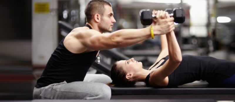 trainer helping woman with a flat bench chest flye