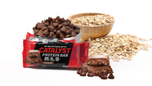 Catalyst Protein Bar in wrapper and unwrapped, and a bowl of chocolate chips and one of oats