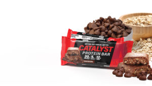 Catalyst Protein Bar chocolate wrapped and unwrapped with a bowl of chocolate chips and a bowl of oats