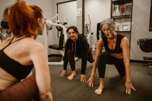 People in a gym performing a forward lunge stretch