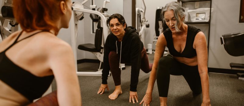 People in a gym performing a forward lunge stretch