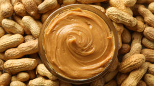 Open jar of natural peanut butter surrounded by shelled peanuts