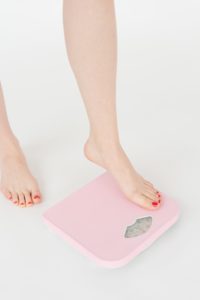 Woman with painted toenails stepping onto a pink scale