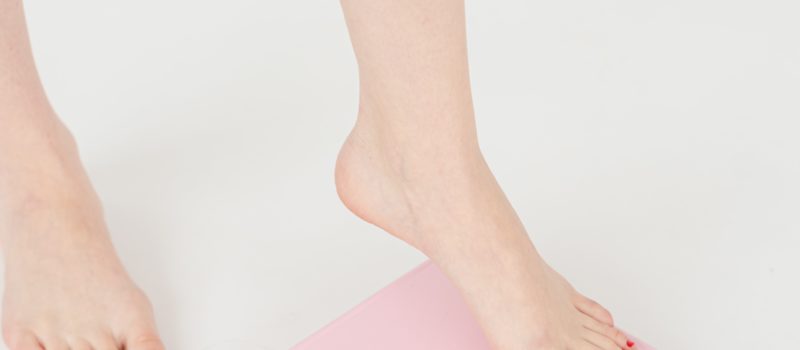 Woman with painted toenails stepping onto a pink scale