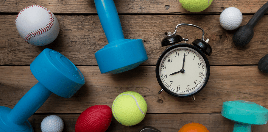 An alarm clock surrounded by sports balls and dumbbells