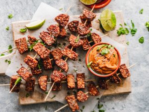 Tempeh on skewers sprinkled with sesame seeds and a bowl of peanut sauce