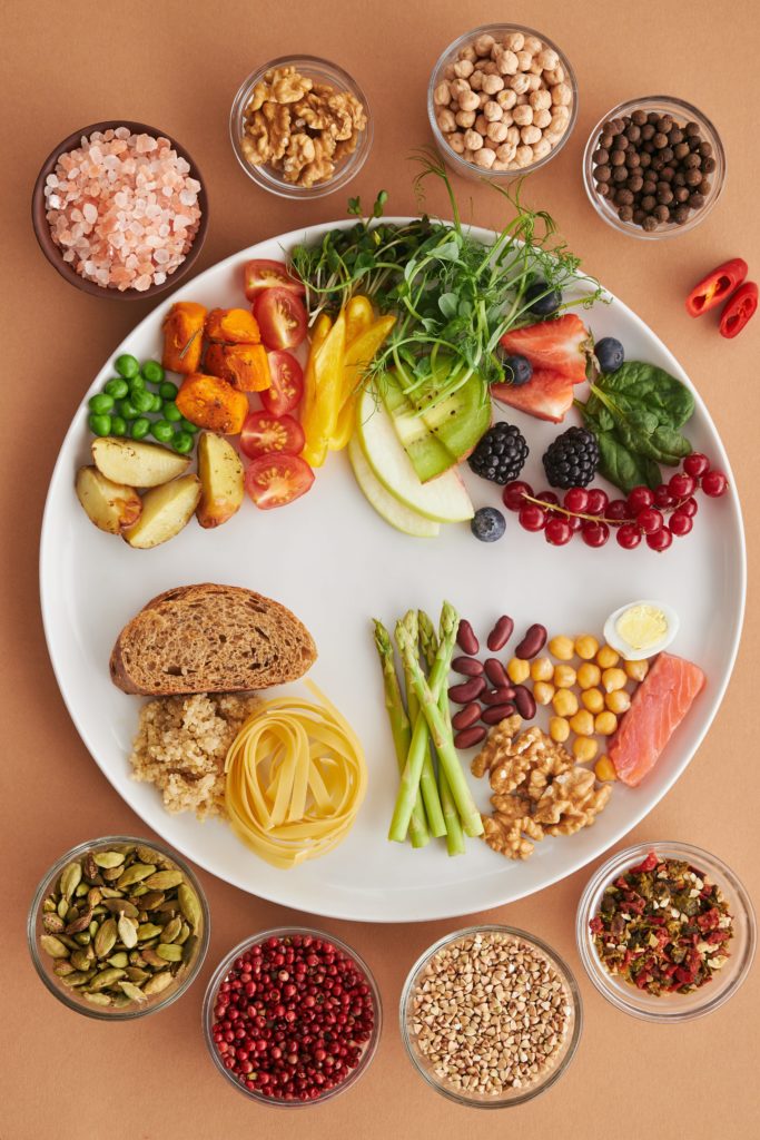 White platter with a variety of healthy foods surrounded by small bowls of nuts, berries, and other nutritious foods