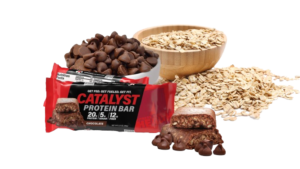 Catalyst Protein Bar wrapped and unwrapped, next to a bowl of chocolate chips and a bowl of oats