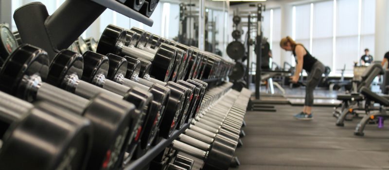 A rack of dumbbells in a gym with non-descript people in the background