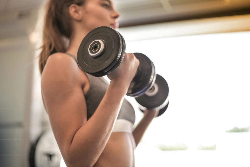 A woman in a sports bra holding dumbbells in the up position of a dumbbell curl