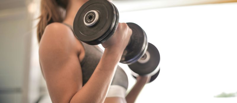 A woman in a sports bra holding dumbbells in the up position of a dumbbell curl