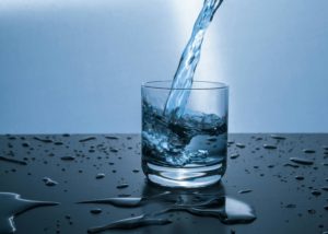 Water being poured into a short glass on a table that has drops of water beading on it