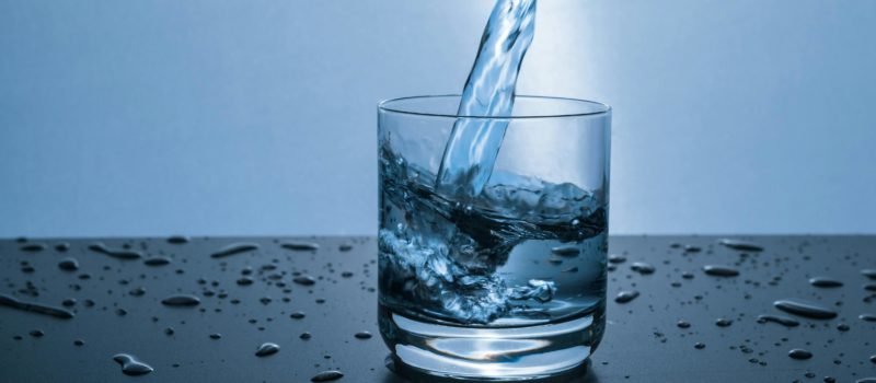 Water being poured into a short glass on a table that has drops of water beading on it